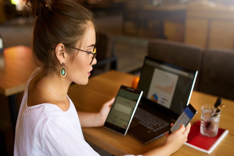 Mujer mirando las pantallas de una tablet, un ordenador portátil y un teléfono.